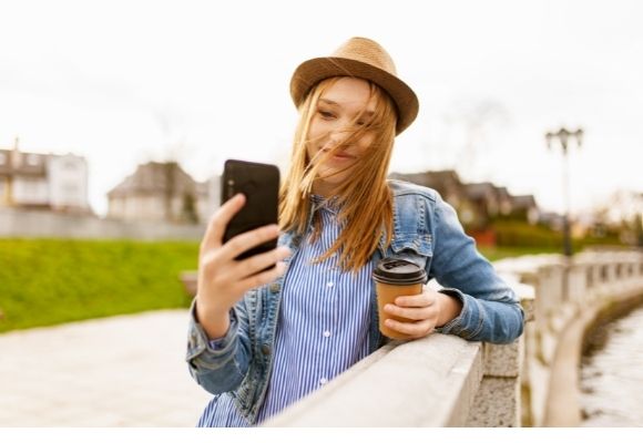mulher de chapéu marrom e casaco jeans tirando selfie